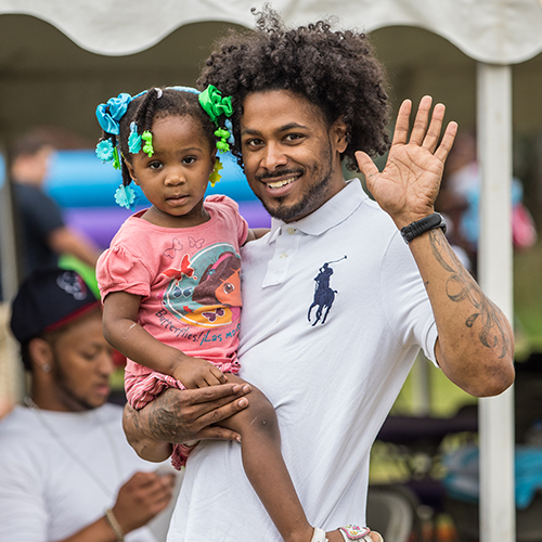A father is holding his daughter and waving at the camera.