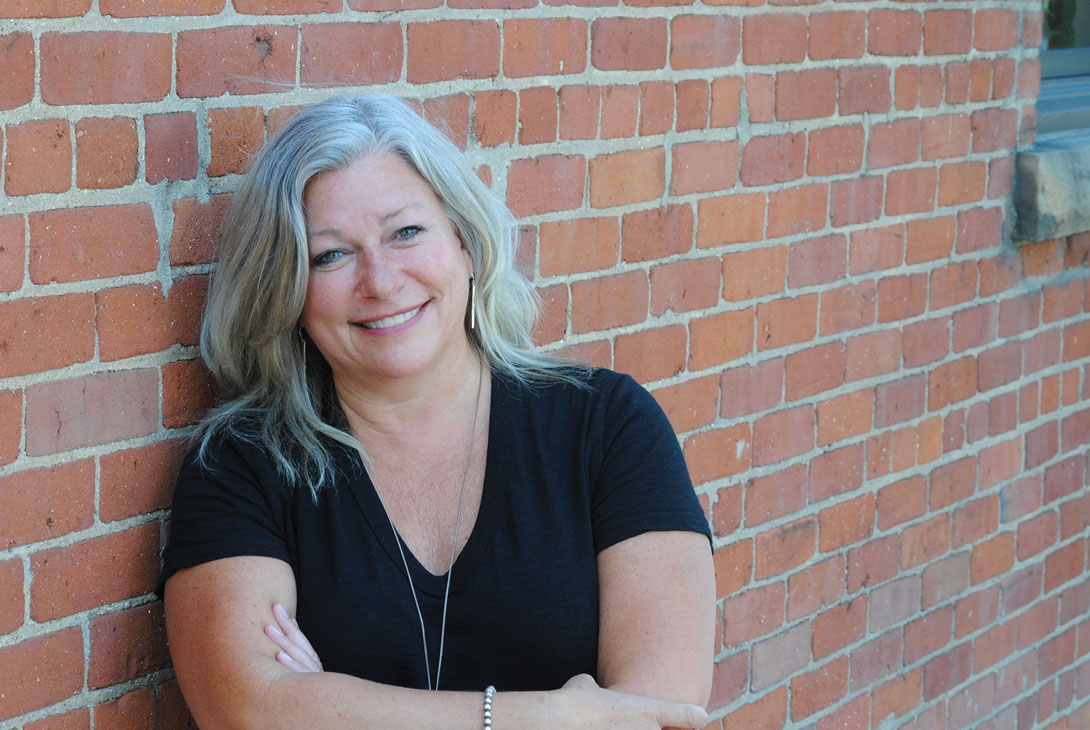 Image of Heather Isch leaning on a brick wall smiling at the camera.